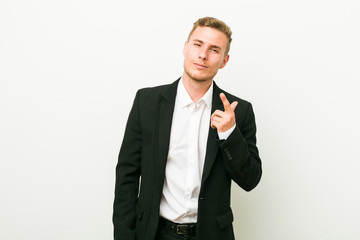 Young caucasian business man pointing with finger at you as if inviting come closer.
