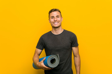 Young caucasian man holding a mat happy, smiling and cheerful.