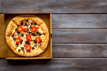 Order pizza to home or office. Italian food in box on dark wooden background top view copy space