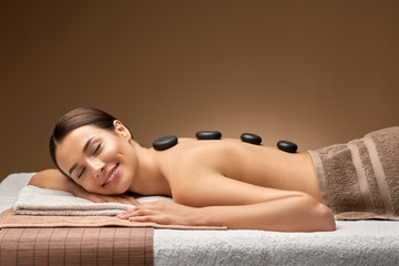 wellness, beauty and relaxation concept - smiling beautiful young woman having hot stone massage at...