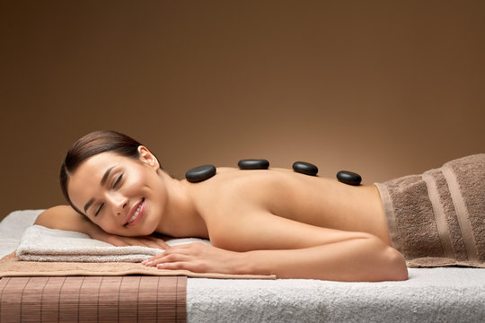 wellness, beauty and relaxation concept - smiling beautiful young woman having hot stone massage at spa