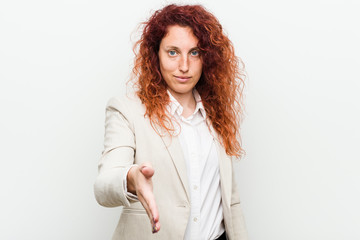 Young natural redhead business woman isolated against white background stretching hand at camera in greeting gesture.