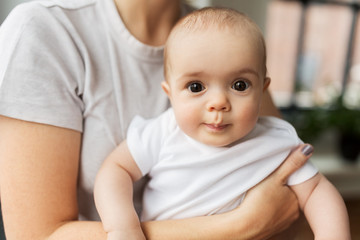 family, child and parenthood concept - close up of young mother holding little baby daughter over grey background