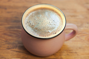 A cup of coffee with beautiful foam on a brown wooden background. Warm colors, stylish toning.