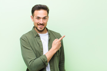 young handsome man looking excited and surprised pointing to the side and upwards to copy space