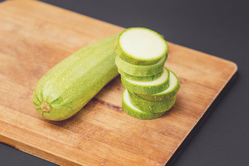 Fresh raw green courgette or zucchini whole and sliced on a wooden cutting board on the black background.