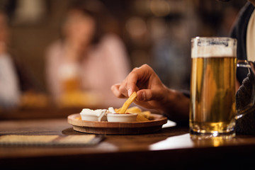 Close-up of man eating French fries while drinking beer in a pub.