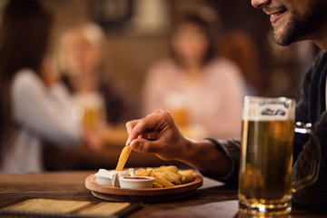 Close-up of happy man enjoying in French fries and beer in a tavern.
