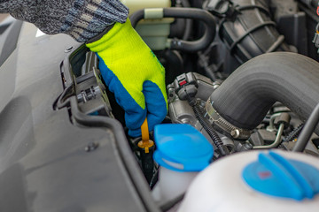 A male hand in a yellow glove holds the lid. checking the oil level