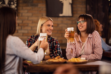 Young happy women toasting with beer and having fun in a pub.