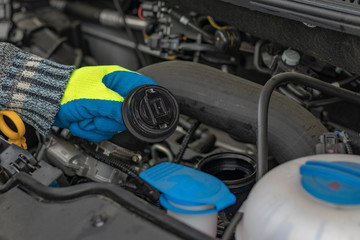 A male hand in a yellow glove holds the lid. checking the oil level