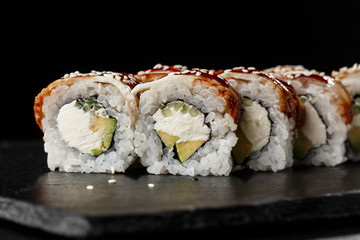 Sushi Rolls with cucumber, avocado, eel and Cream Cheese inside on black slate isolated. Philadelphia unagi roll sushi with shrimp. Sushi menu. Horizontal photo.