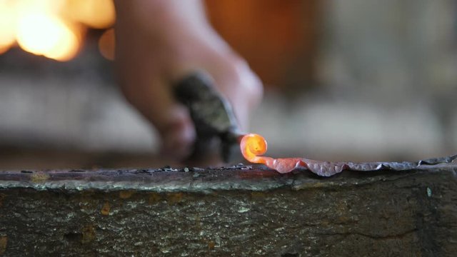 Master's hands twisting a metallic red rod in a metallic rose head in a workshop