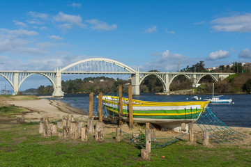 A fisher boat outside the water in the beach with a big bridge behind it