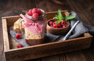 No-bake layered dessert with dark chocolate mousse, crushed cookies and raspberry cream cheese in glass jar