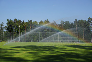 stationäre Rasensprenger auf dem Sportplatz erzeugen Regenbogen 