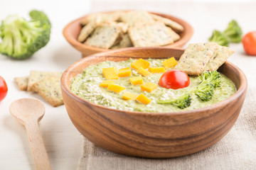 Green broccoli cream soup with crackers and cheese in wooden bowl on a white wooden background. side view, selective focus.