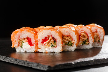 Sushi Rolls with flying fish caviar , fried onion, salmon and Cream Cheese inside and on black slate isolated. Philadelphia roll sushi with shrimp. Sushi menu. Horizontal photo.