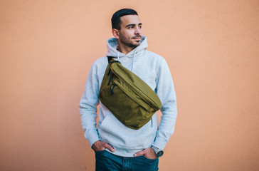 City portrait of handsome hipster guy wearing gray blank hoodie with big waist bag with space for...