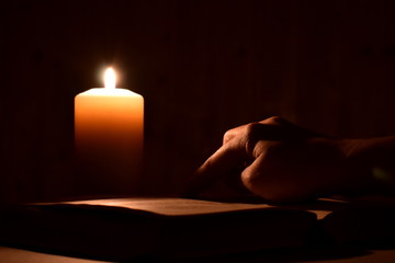Obraz na płótnie Canvas Reading bible in dark with candle. Finger on book at night. A person reads a mysterious book in darkness.