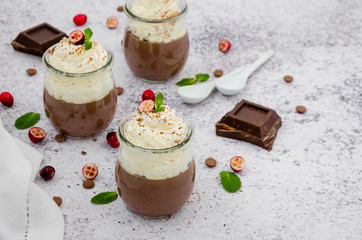 Chocolate cream on agar agar with whipped cream on top in glass jars on a light stone background.