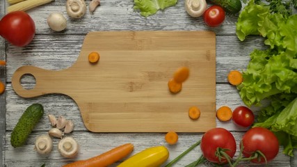Slow motion shot of sliced carrot falling on wooden chopping board and spreading over kitchen table with mushrooms and vegetables - Powered by Adobe