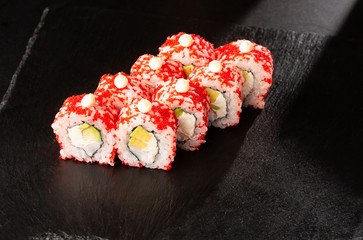 Sushi Rolls with avocado, shrimp and cream cheese inside on black slate isolated. California rolls covered orange tobiko or masago caviar. Sushi menu. Horizontal photo.