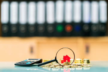 Magnifying glass with red home model put on gold coin and calculator and gold coin for select in the office, Loan for business investment the real estate and buy house to family in the future concept.