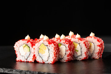 Sushi Rolls with avocado, shrimp and cream cheese inside on black slate isolated. California rolls covered orange tobiko or masago caviar. Sushi menu. Horizontal photo.