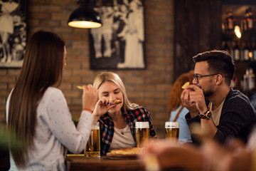 Group of happy friends drinking beer and eating in a pub.