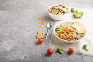 Green broccoli cream soup with crackers in white bowl on a gray concrete background, side view, copy space.