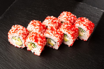 Sushi Rolls with avocado, eel, cucumber and cream cheese inside on black slate isolated. California rolls covered orange tobiko or masago caviar. Sushi menu. Horizontal photo.