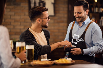 Happy man making contactless payment to a waiter in a pub.