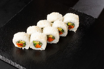 Sushi Rolls with avocado , cucumber, green onion and carrot inside on black slate isolated. Vegan california rolls covered white sesame seeds. Sushi menu. Horizontal photo.