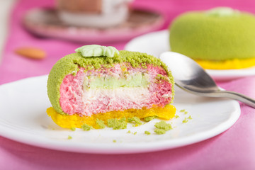 Green mousse cake with pistachio and strawberry cream on a pink textile background. side view, selective focus.