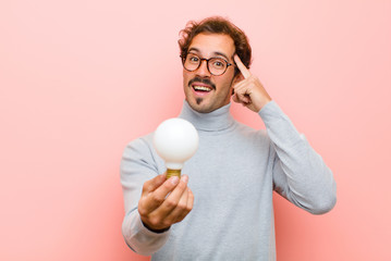 young handsome man having an idea with a light bulb against pink flat wall