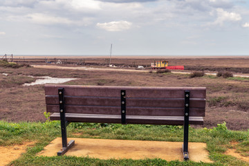 A bench with a view towards some boats in the River Hun, seen in Thornham Old Harbour, Norfolk,...