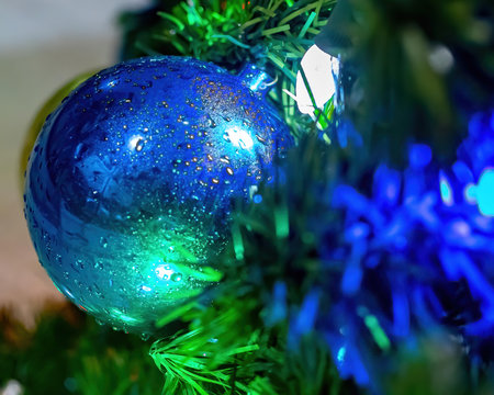 Blue Holiday Ornament On The Tree With Lights Behind It 