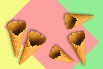 Waffle cones for ice cream on a light yellow, sweet pink and light green background with copy space for insertion or decoration of text, logo or wording, concept of colorful summer cold sweet snacks