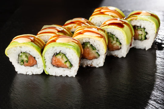 Green dragon sushi roll with salmon, cucumber and avocado. Japanese food. Traditional asian rice sushi healthy seafood. Black background. Horizontal photo.