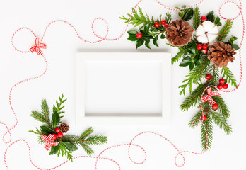 Christmas composition  with photo frame, cotton flower, branches of spruce and holly with red berries on white background. Merry christmas greeting card with empty space for holiday text.