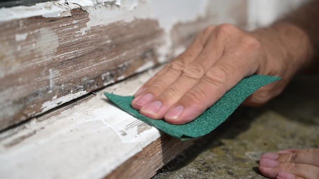 Slow motion shot of a man's hand sanding the edge of a worn window sill