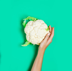 Female hand holding broccoli on green background.