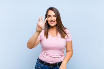 young pretty woman smiling and looking friendly, showing number three or third with hand forward,...