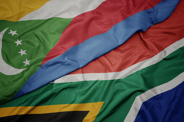 waving colorful flag of south africa and national flag of comoros.