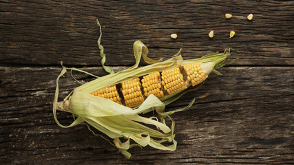 The corncob in the husk is cut into pieces. Corn lies on a table of old wooden boards. Minimalism
