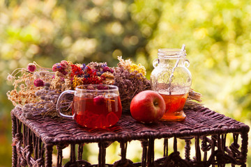 Cup of tea, jar of jam and apple in front of dried flower bunch 
