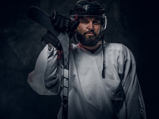 Professional hockey player in helmet is posing with hockey stick at photo studio.