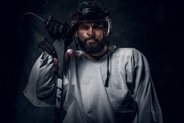 Professional hockey player in helmet is posing with hockey stick at photo studio.
