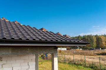 The roof of a single-family house covered with a new ceramic tile in anthracite, against the blue sky.